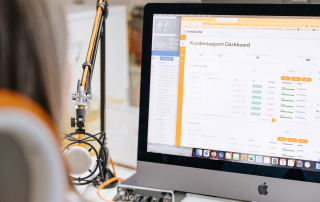 Mitarbeiterin von immoGrafik arbeitet am iMac mit geöffnetem Kundensupport-Dashboard zur Verwaltung von Exposé-Plänen
