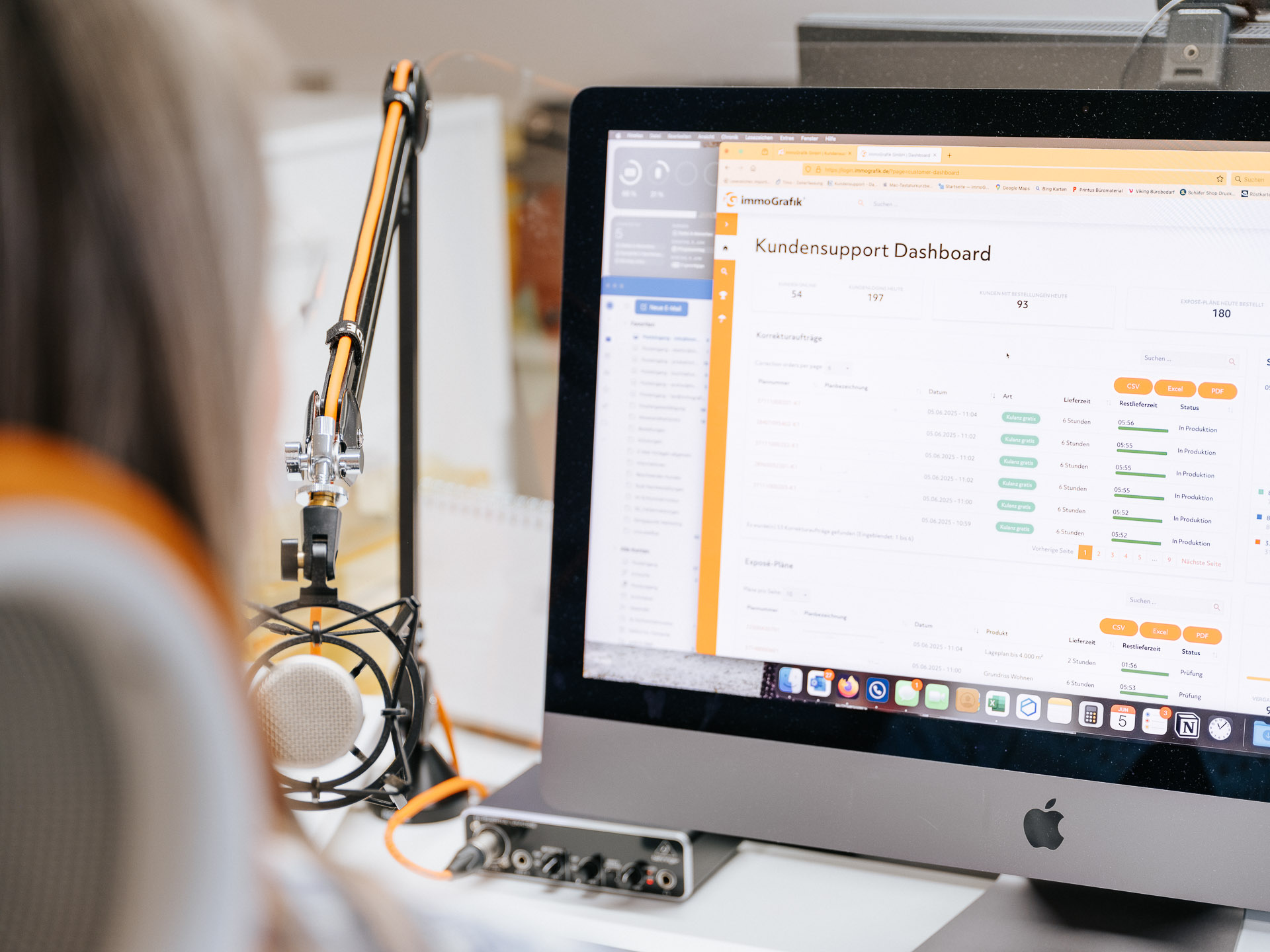 Mitarbeiterin von immoGrafik arbeitet am iMac mit geöffnetem Kundensupport-Dashboard zur Verwaltung von Exposé-Plänen