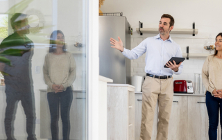 Ein Berater erklärt einem Paar und einer weiteren Person in einem hellen, modernen Innenraum professionelle Grundrisslösungen, die für Klarheit, Effizienz und emotionale Wirkung bei Exposé-Plänen stehen.