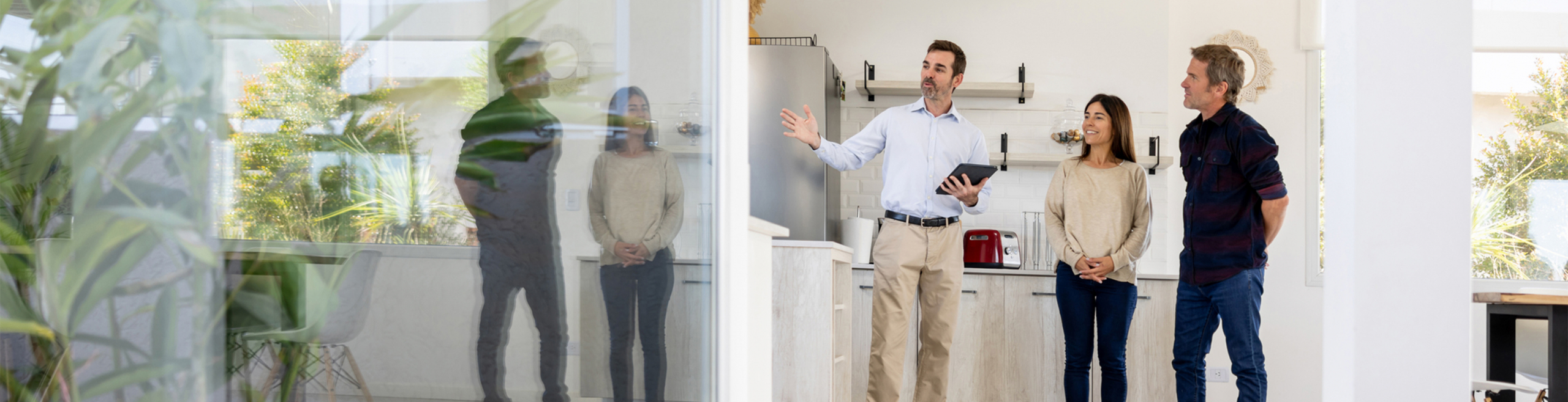 Ein Berater erklärt einem Paar und einer weiteren Person in einem hellen, modernen Innenraum professionelle Grundrisslösungen, die für Klarheit, Effizienz und emotionale Wirkung bei Exposé-Plänen stehen.